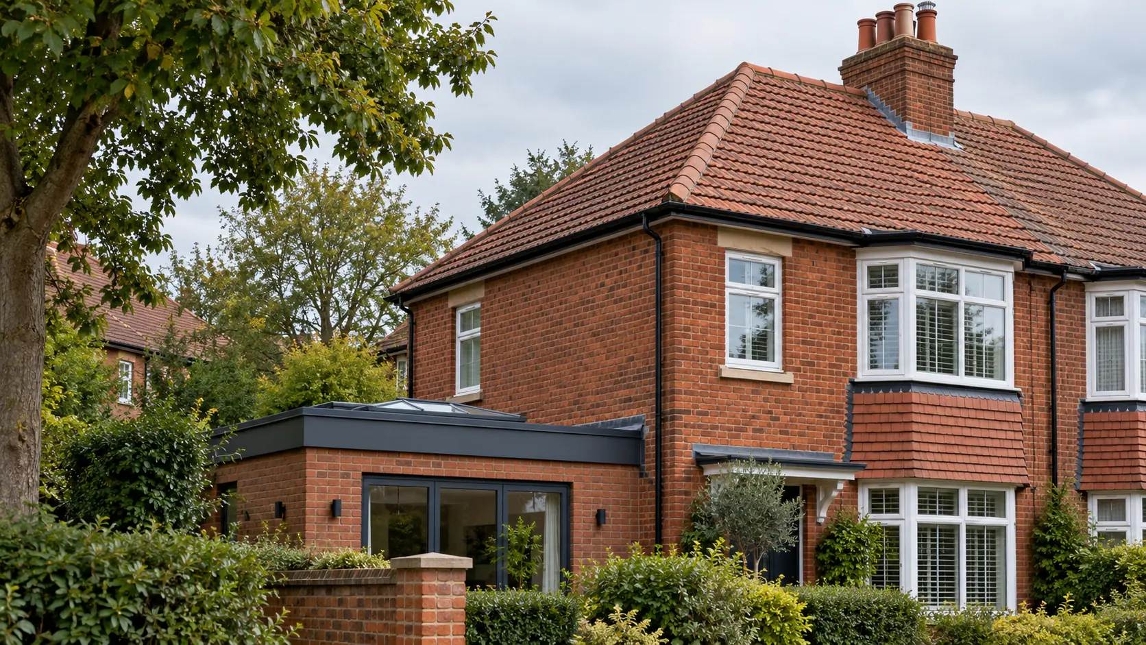 A red-brick semi-detached house with a tiled hipped roof, a chimney stack and a flat-roofed extension